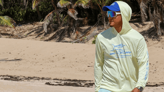 Man wearing AQWA lightweight hoodie and blue cap, walking on the beach.