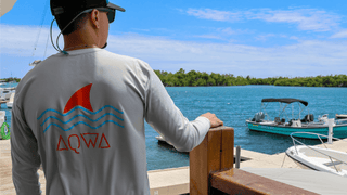 Man wearing AQWA performance fishing shirt with shark fin design at the marina.