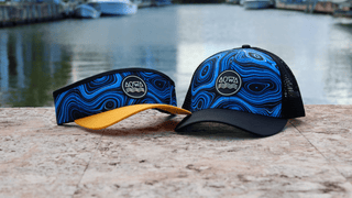 AQWA trucker hat and visor with blue ocean-inspired design, displayed near the water.