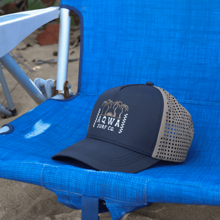 AQWA navy and khaki trucker hat resting on a beach chair, capturing relaxed coastal vibes.