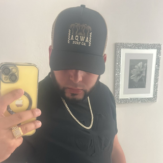 AQWA black trucker cap with beige palm tree logo, worn with casual black outfit — blending surf aesthetic with urban streetwear style.