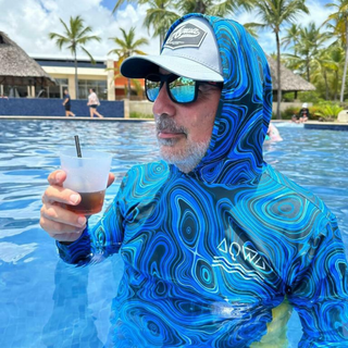 AQWA blue topographic rash guard with hoodie, worn in pool by man enjoying sunny resort day — tropical comfort and protection.