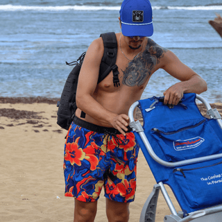 AQWA floral swim trunks in action by the beach, paired with a blue cap — perfect for an energetic coastal lifestyle.