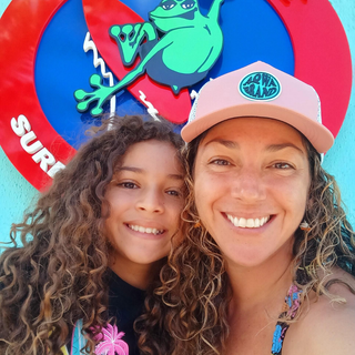 AQWA pink mesh cap worn by woman with child at surf school — coastal smiles and family beach lifestyle.