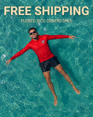 Smiling man relaxing in crystal-clear turquoise Caribbean water wearing a red AQWA long sleeve performance shirt and black swim shorts — lightweight beachwear designed for island adventures, boating, and sun protection.