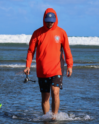 AQWA red performance hoodie with black side panels, worn by man fishing at the shore — designed for maximum sun protection and coastal comfort.
