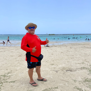 AQWA rash guard in vibrant red with black side panels, worn by man enjoying a sunny beach day in Puerto Rico — designed for UV protection and comfort by the shore.