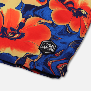 Close-up of AQWA rubber logo patch on bottom leg of floral swim trunks – bold branding on high-performance fabric.