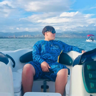 AQWA topographic blue rash guard and matching shorts worn by man seated on a boat — performance comfort for ocean adventures.