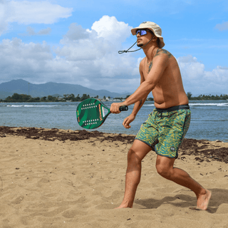 AQWA green wavy swim trunks worn during beach paddle match — comfort meets style under the sun.