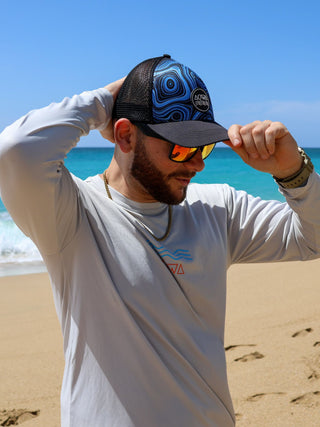 Man putting on an AQWA hat while wearing a rash guard, on a beach paradise