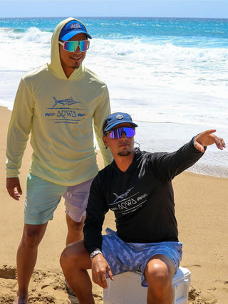 Two men at the beach looking for adventure, while both are wearing AQWA hooded rash guards and hats